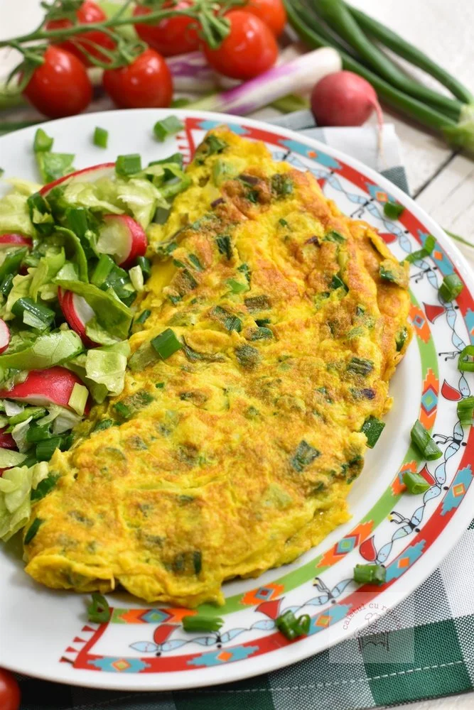 Omletă cu ceapă verde gătită, servită pe o farfurie albă